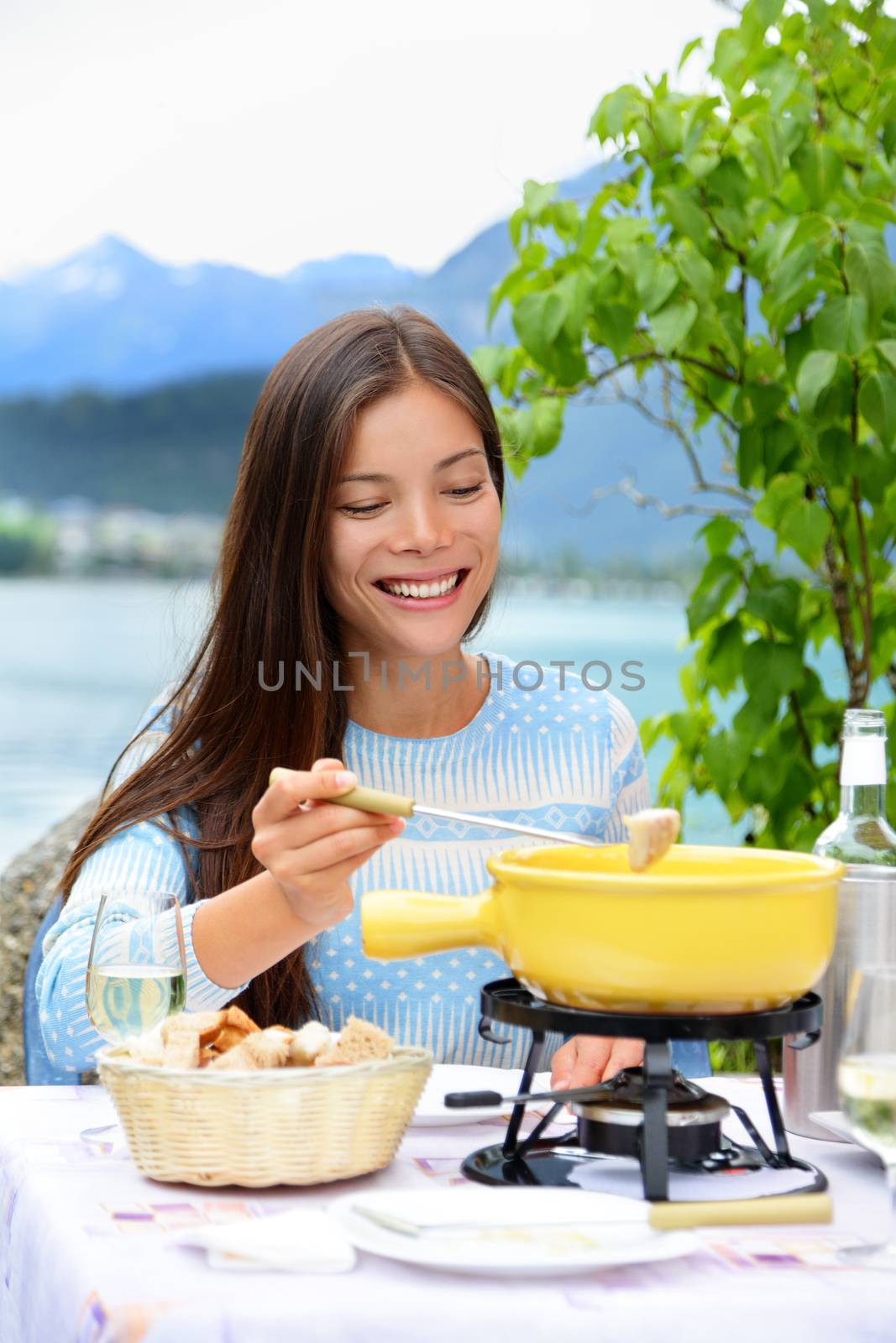 Cheese fondue - woman eating local Swiss food. People eating traditional food from Switzerland having fun by lake in the Alps on travel in Europe.