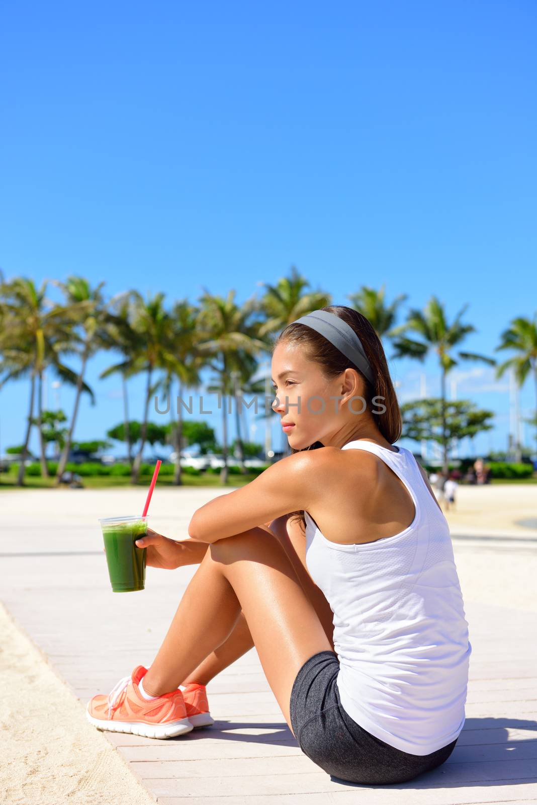 Exercise woman runner drinking green vegetable smoothie resting and relaxing after running. Fitness and healthy lifestyle concept with multiracial Asian Caucasian female model.