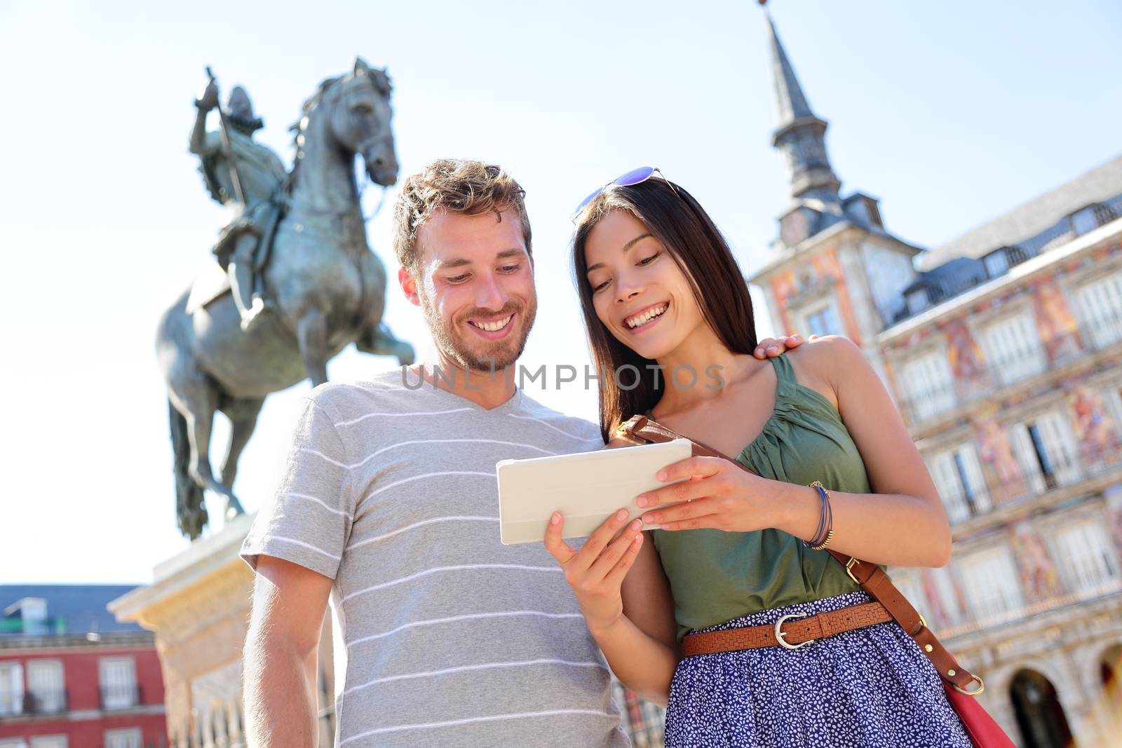 Madrid tourists using tablet travel app guidebook ebook on Plaza Mayor by statue of King Philip III. Tourist couple sightseeing visiting tourism landmarks and attractions in Spain. Young woman and man