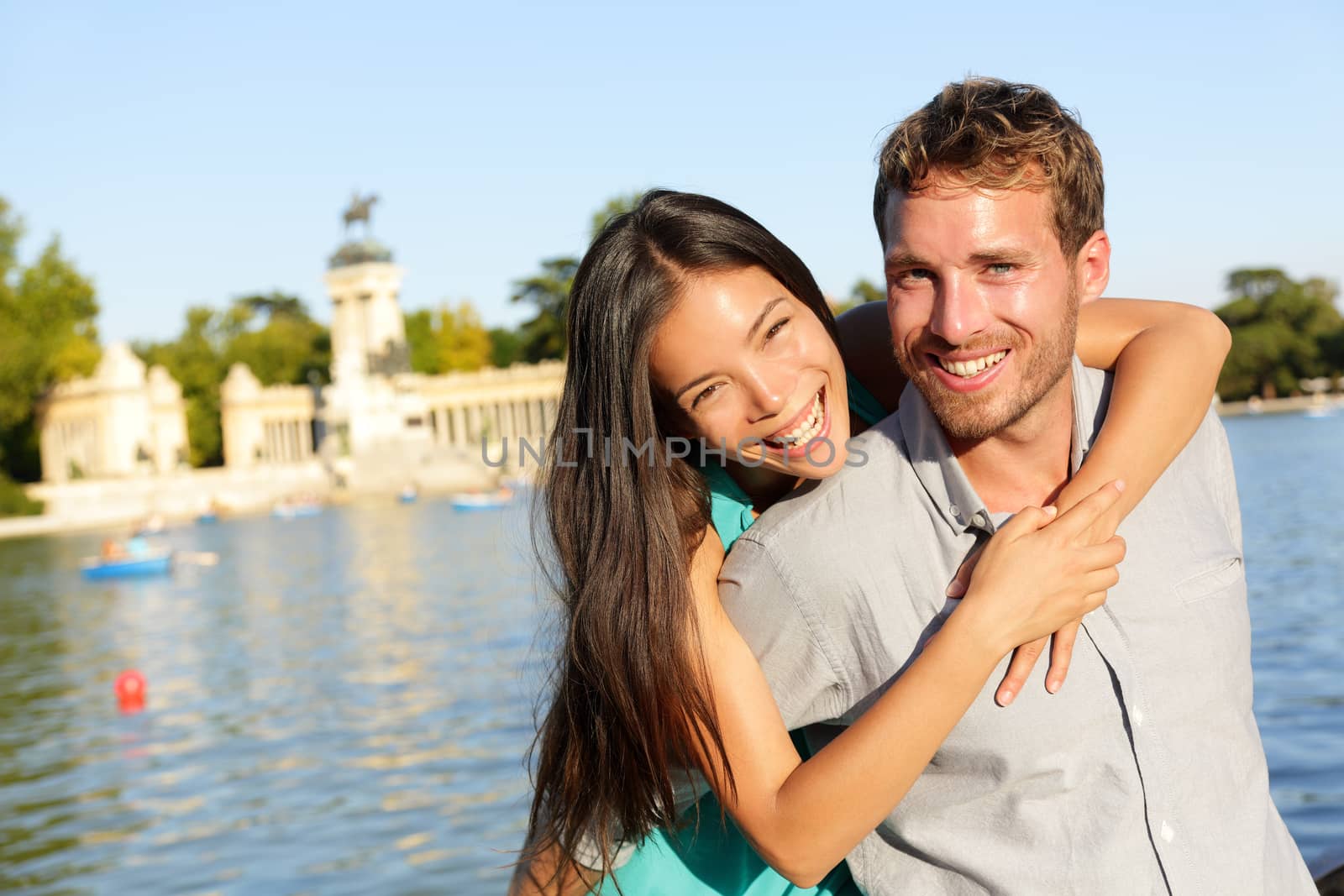 Romantic couple portrait embracing in love looking at camera. Multiracial woman and man smiling happy by lake in El Retiro in Madrid, Spain, Europe.