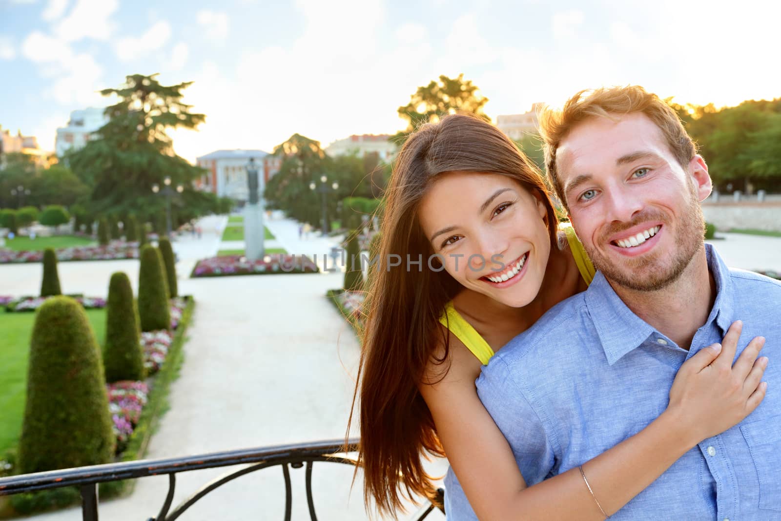 Portrait of Romantic couple embracing in love looking at camera. Multicultural man and woman smiling happy in el Retiro in Madrid, Spain, Europe. Asian girl, young Caucasian man.