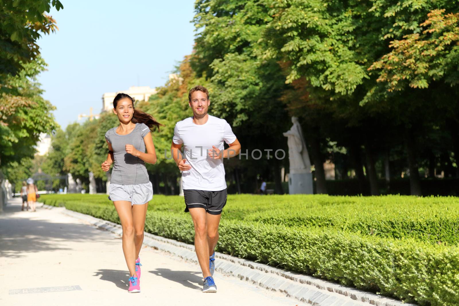 Running couple runners jogging in city park. Exercising woman and man runner training together on run living healthy active lifestyle in Buen Retiro Park, Parque el Retiro in Madrid, Spain, Europe.