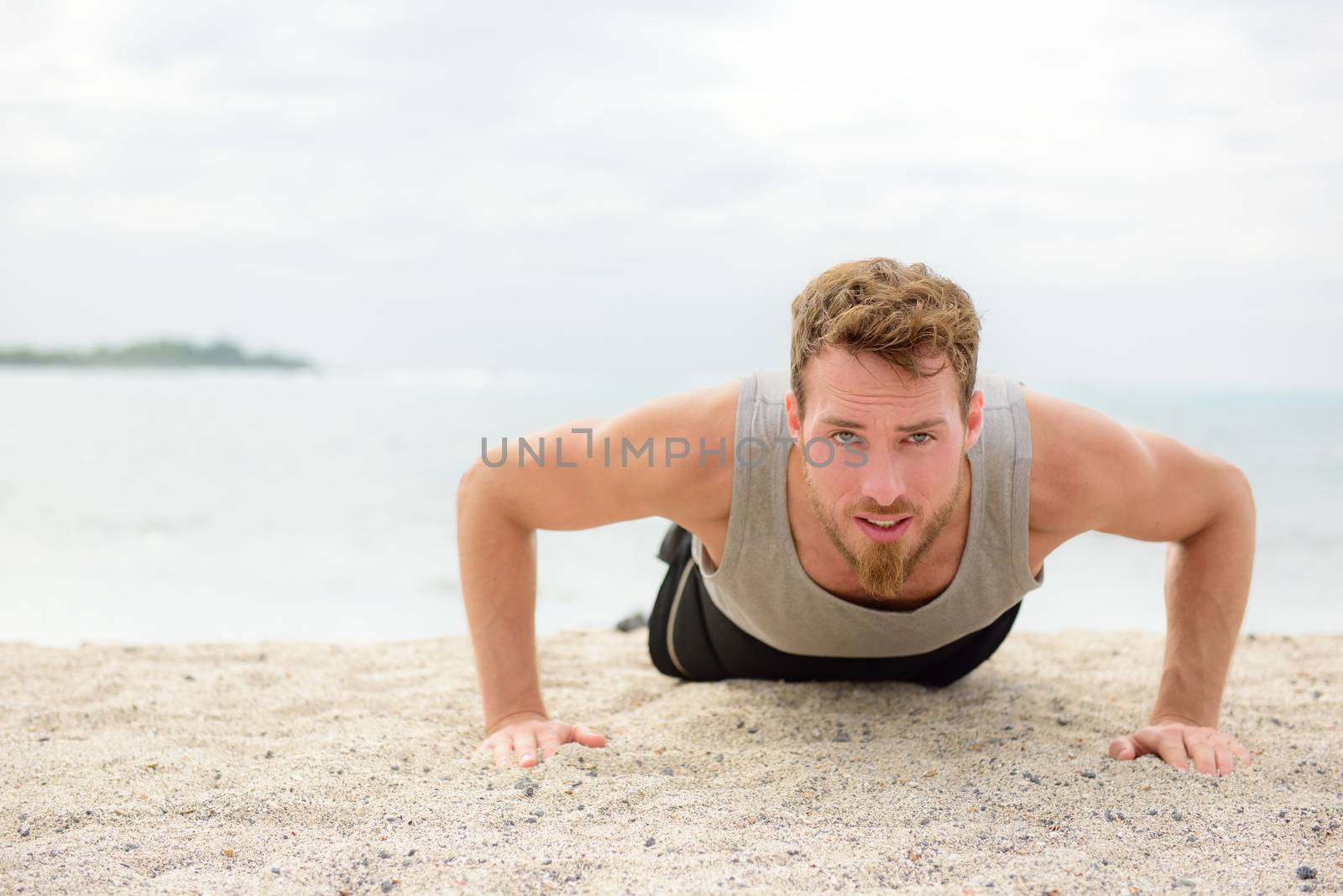 Push-up crossfit man fitness model training pushups on beach outdoors. Fit male fitness trainer working out exercising in summer on beach.