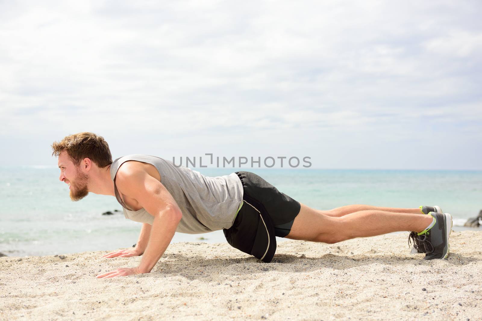 Push-ups - man fitness model training pushups on beach outdoors. Fit male fitness trainer working out exercising in summer on beach.