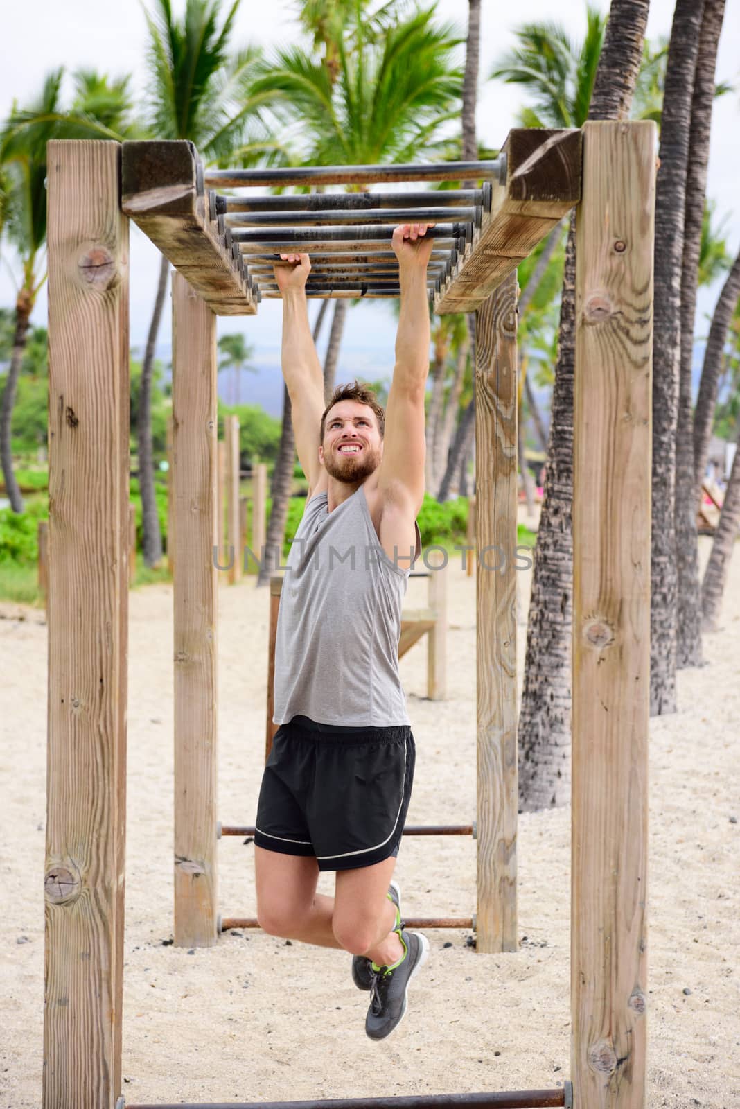 Fitness man on monkey bars fitness station gym. Strong male trainer training on brachiation ladder outdoors equipment as part of crossfit workout routine.