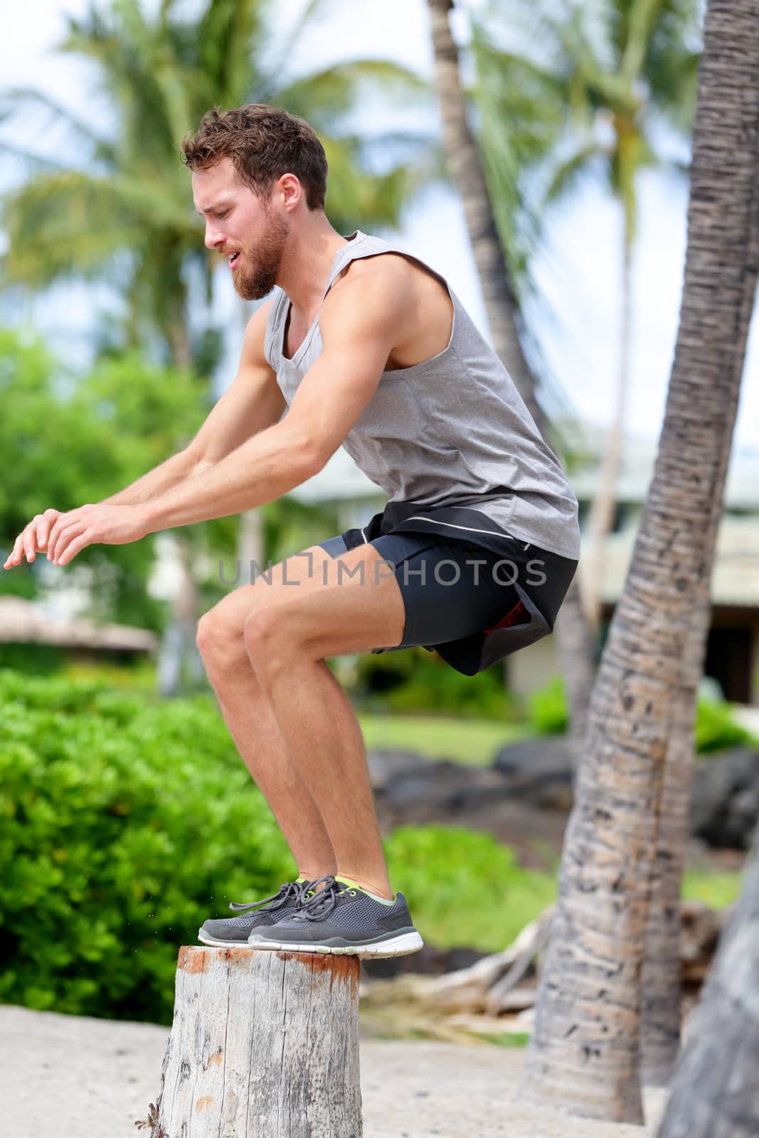 Fitness athlete bench jump squat jumping outside in nature landscape. Strength training fit male working out exercising outdoors on beach in summer doing jumping on tree trunk.