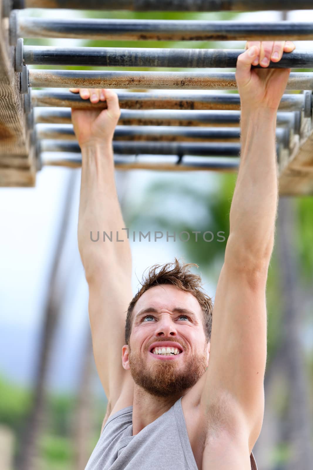 Fit man cross training on monkey bars station. Fitness workout on brachiation ladder in an outdoor gym outside. Male athlete swinging on high bars exercising.