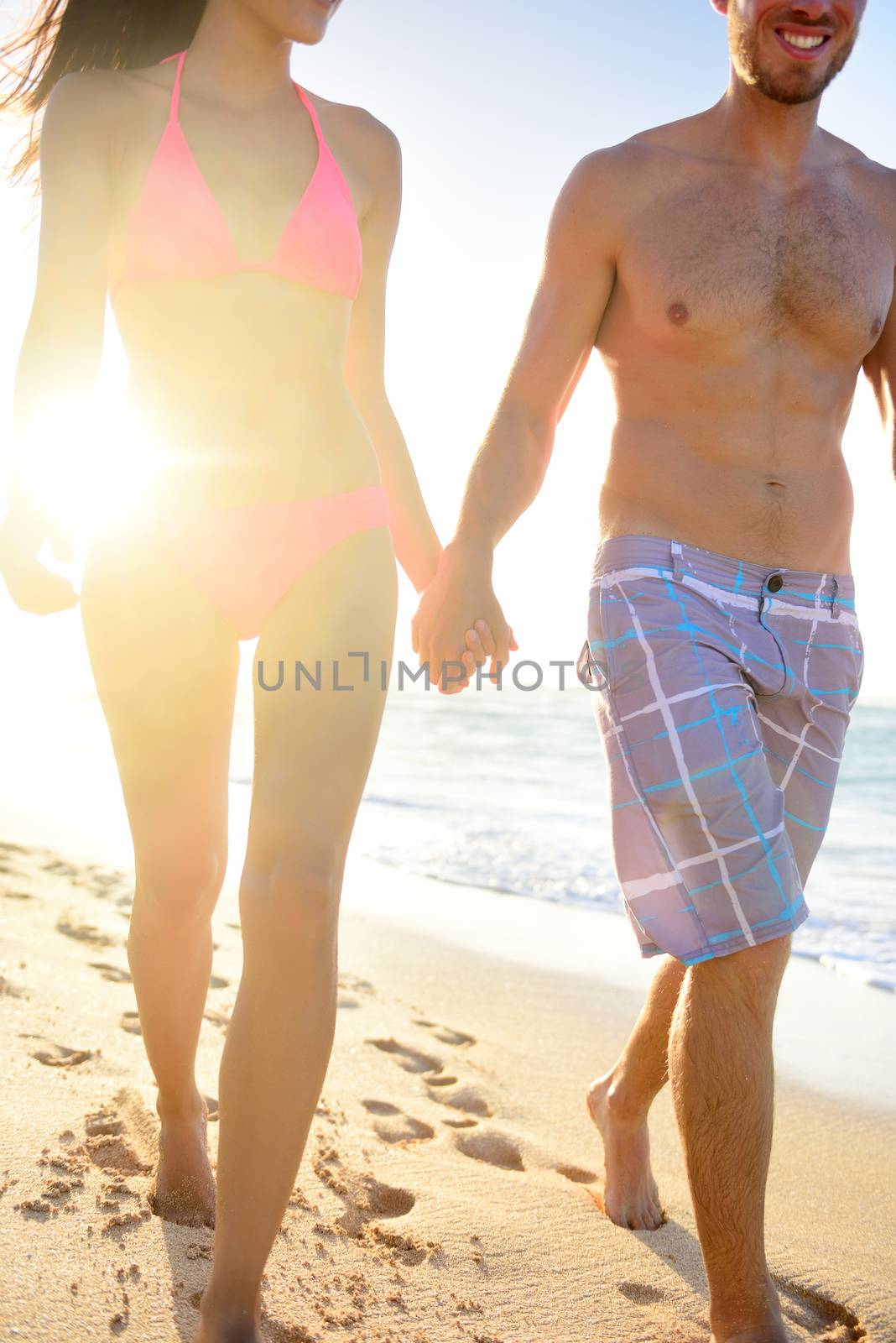Young couple walking in beach sunset happy holding hands man smiling on joyful honeymoon vacation Hawaii summer travel. Body close up.