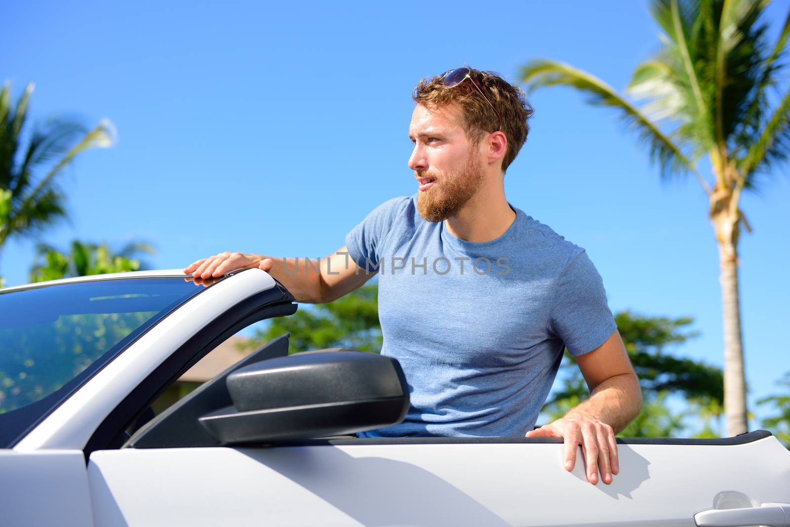 Hipster urban man portrait with cool convertible car on summer road trip. Young adult sitting in his rental new car looking happy.