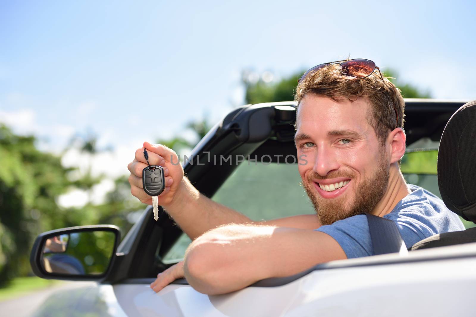 Man driving rental car showing new car keys happy. Young adult excited on road trip with key for cars leasing or rental or purchase.