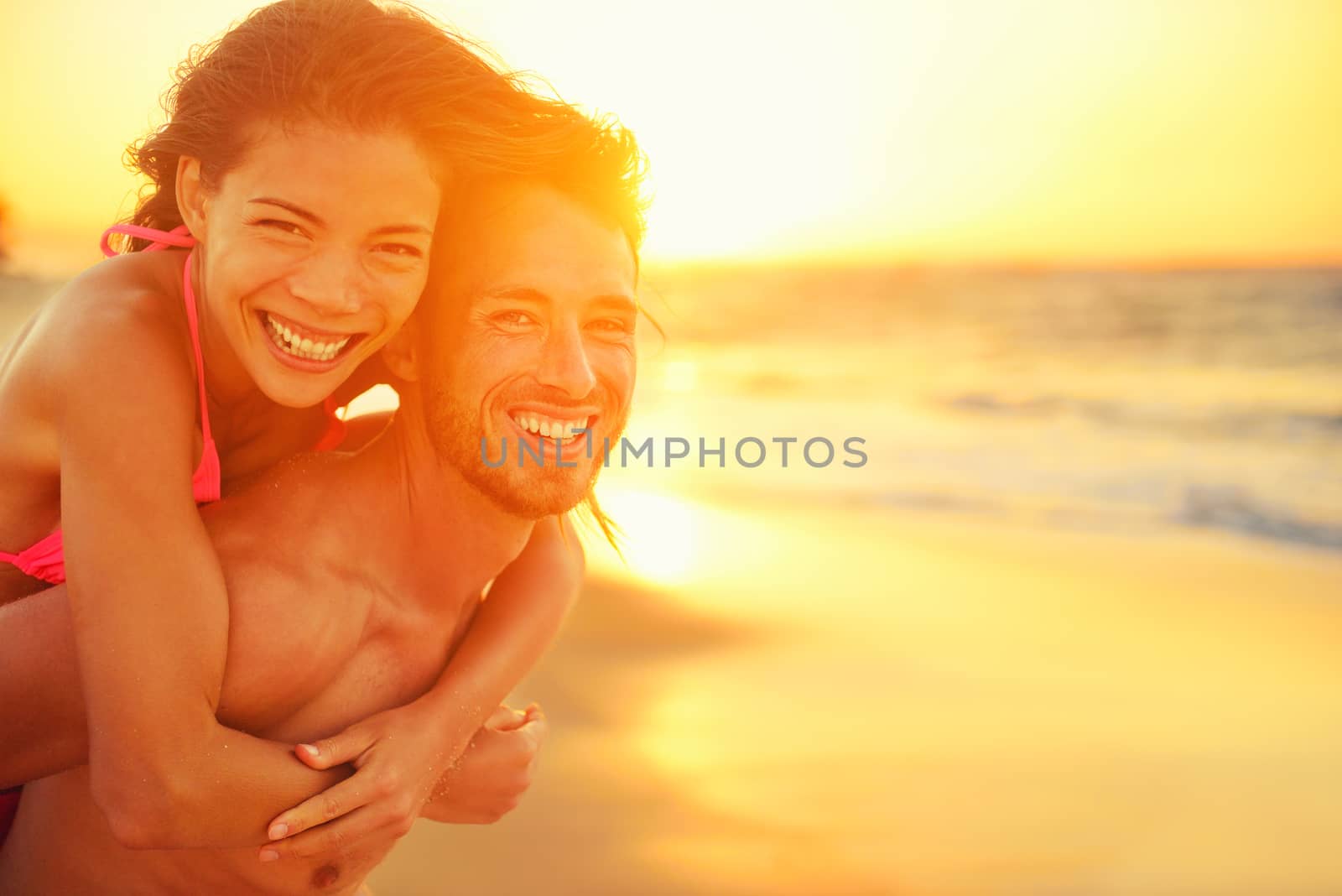Lovers couple in love having fun dating on beach portrait. Beautiful healthy young adults girlfriend piggybacking on boyfriend hugging happy. Multiracial dating or healthy relationship concept.