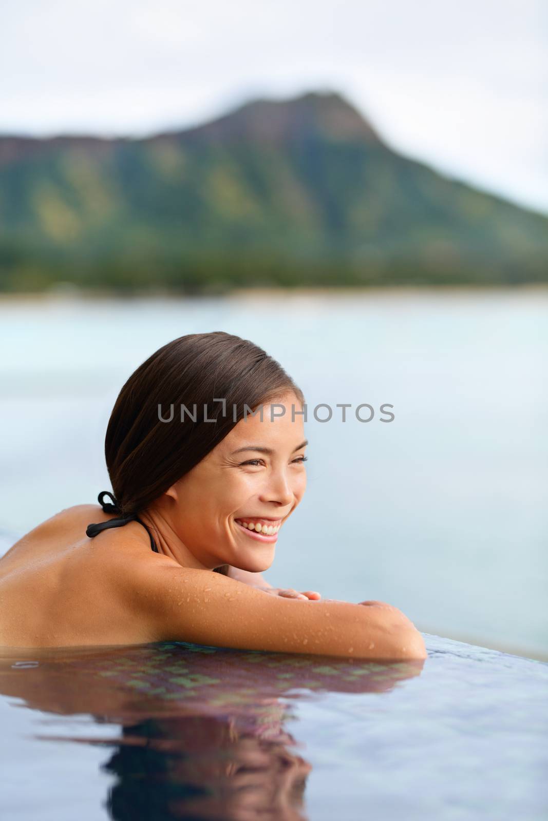 Holiday woman swimming at beach on Hawaii travel. Asian chinese young lady relaxing in infinity pool in luxury hotel resort on Waikiki beach in Honolulu, Oahu, Hawaii, USA.