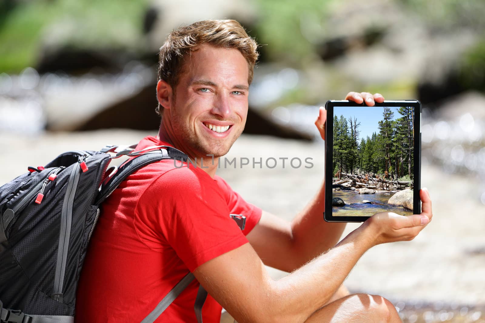 Hiking man showing nature forest picture on tablet by Maridav