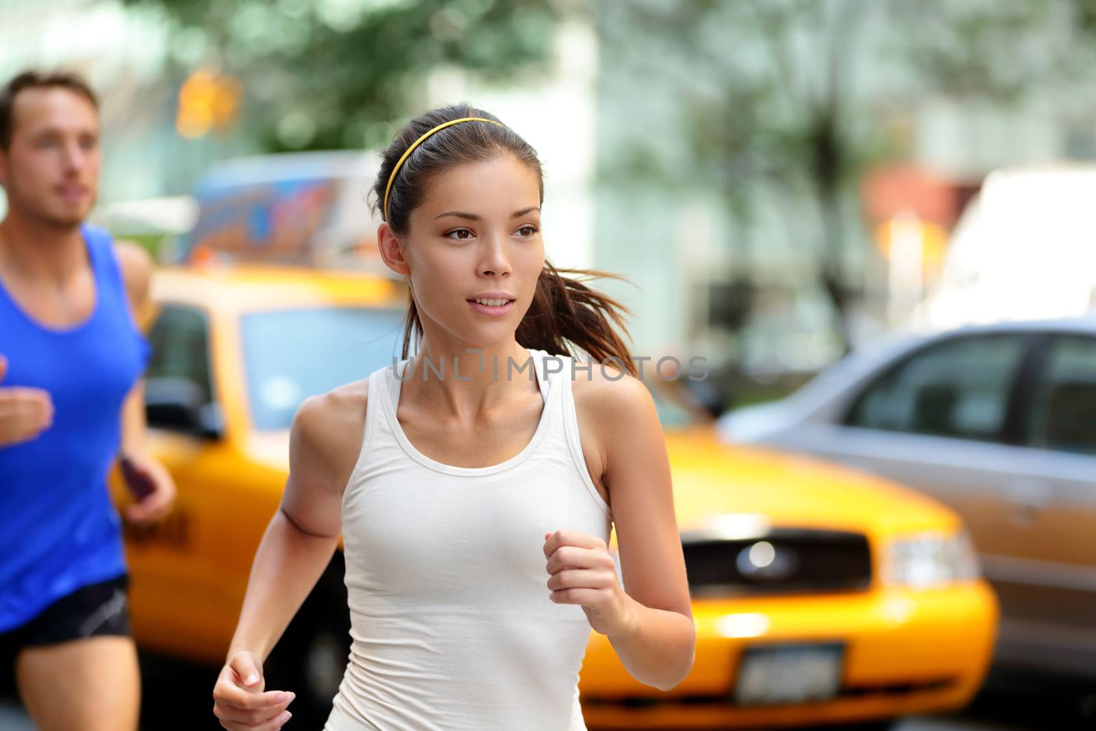 Active people jogging on New York city street, NYC. Young asian female runner and caucasian man running together training in Manhattan busy traffic with yellow taxi cabs in summer.