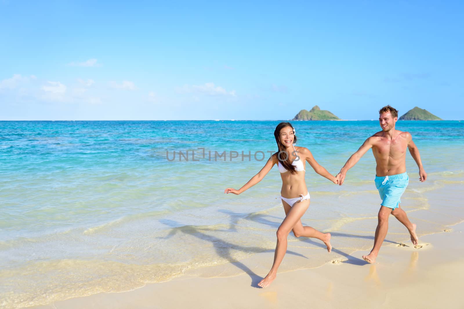 Beach vacations - happy couple running together joyful in water during holidays in Hawaii.