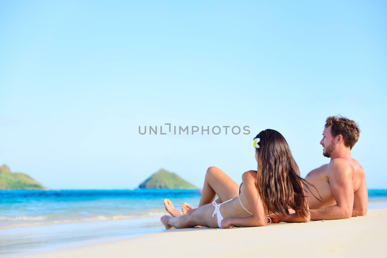 Beach sun tan couple relaxing on holiday in Hawaii. Vacations holidays suntan concept - adults lying down tanning on luxury exclusive beach in Lanikai, Oahu, Hawaii, USA.