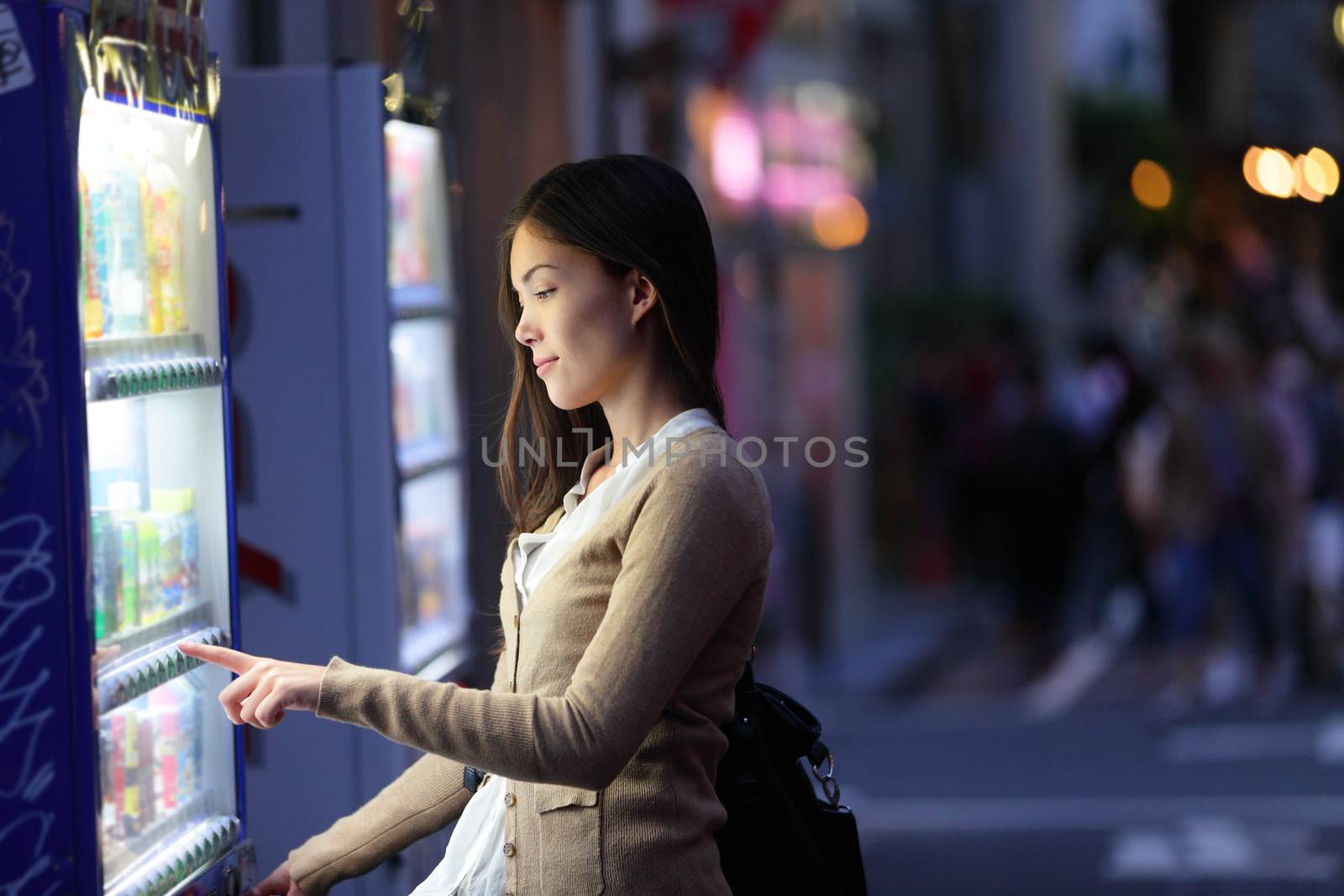 Japan vending machines - Tokyo woman buying drinks. Japanese student or female tourist choosing a snack or drink at vending machine at night in famous Harajuku district in Shibuya, Tokyo, Japan.