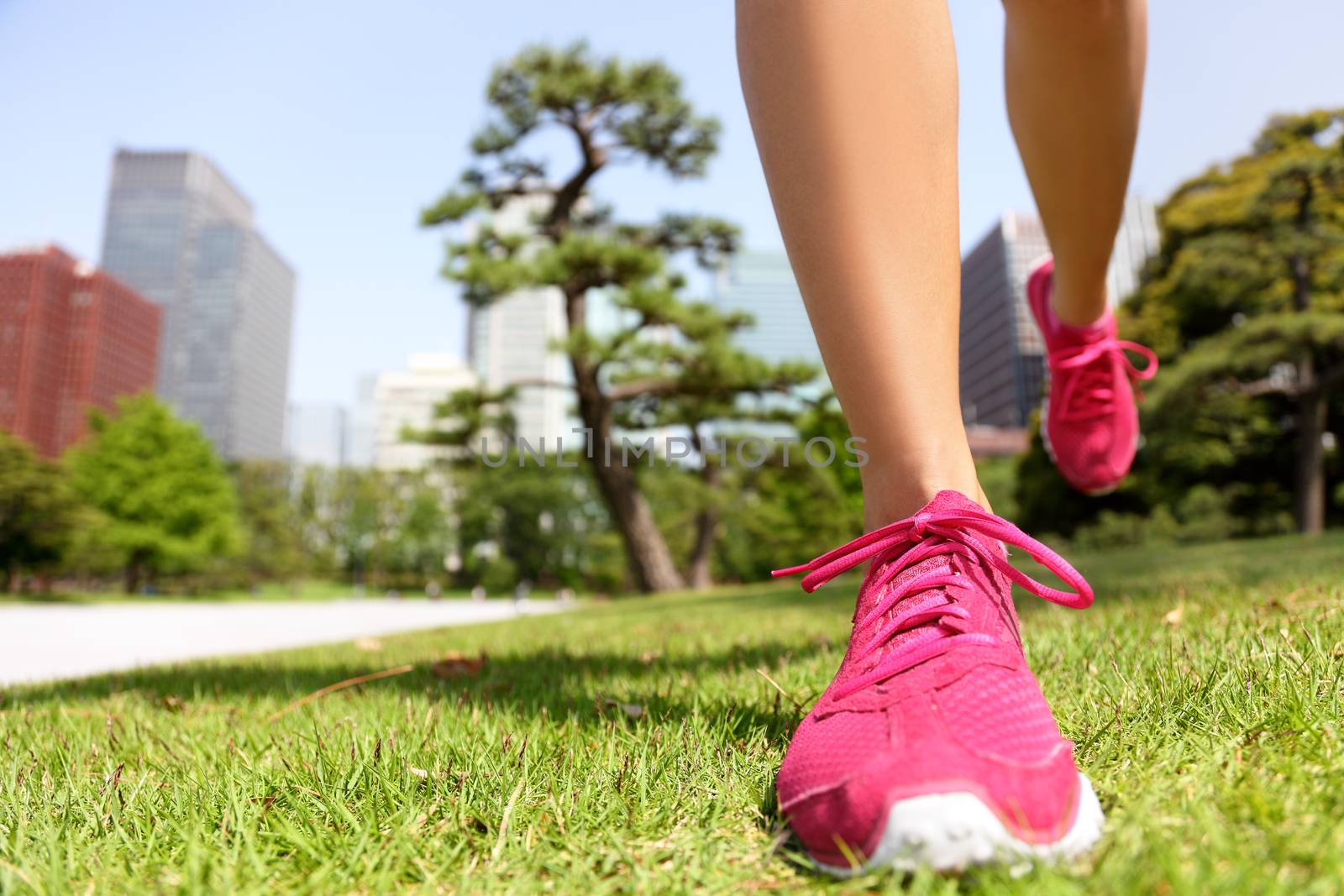 Running shoes - woman runner jogging staying fit in Tokyo Park, Japan. Closeup of pink trainers in green grass in summer park near the Imperial Palace and Ginza district downtown.