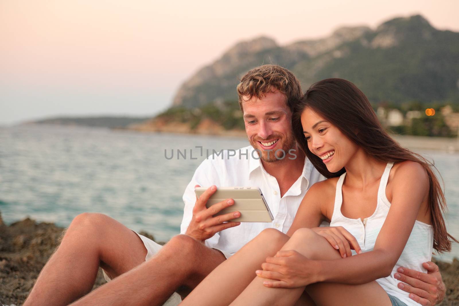 Romantic couple relaxing on beach using tablet app by Maridav