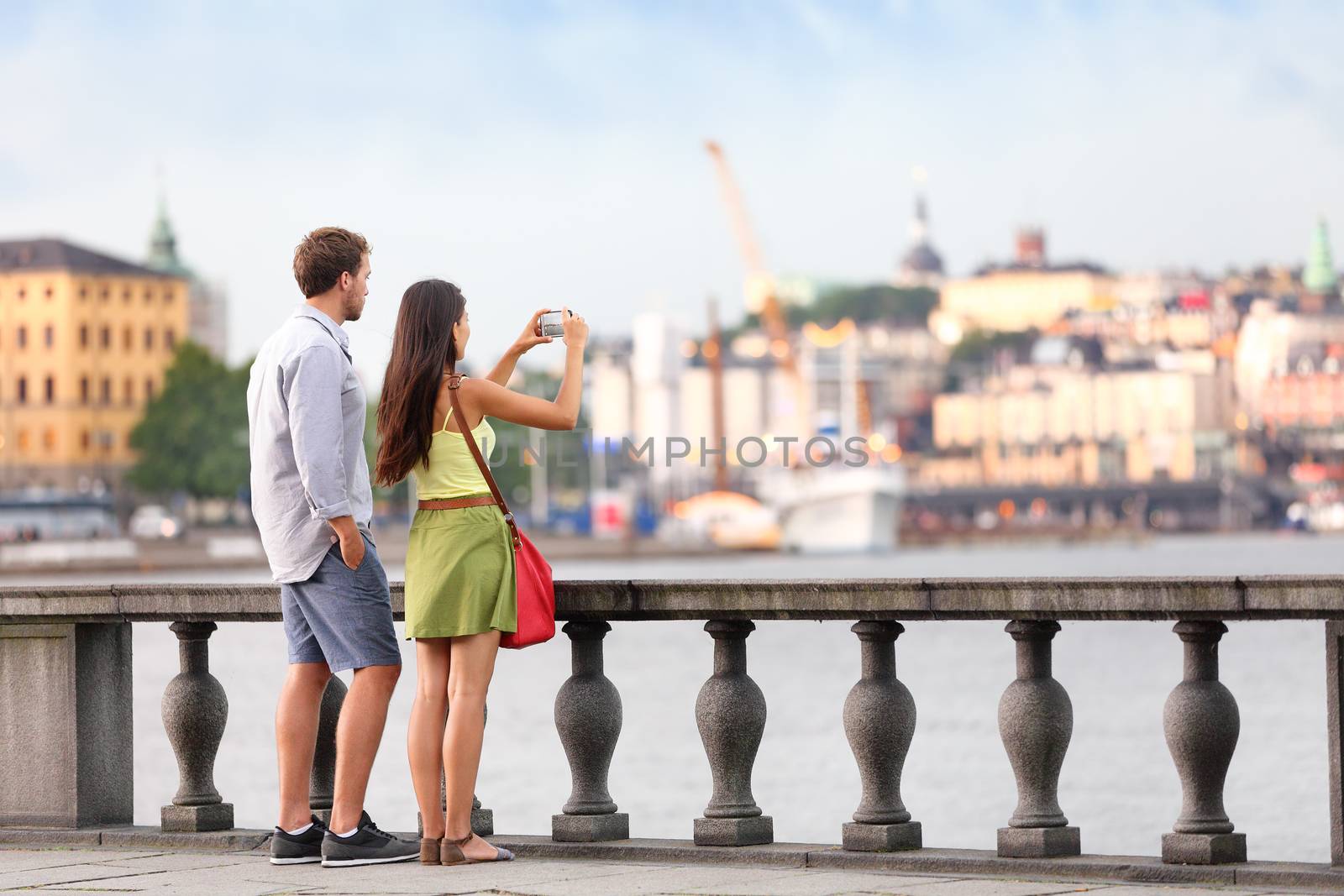 Europe travel tourist people taking pictures. Tourists couple in Stockholm taking smartphone photos having fun enjoying skyline view and river by Stockholm's City Hall, Sweden.