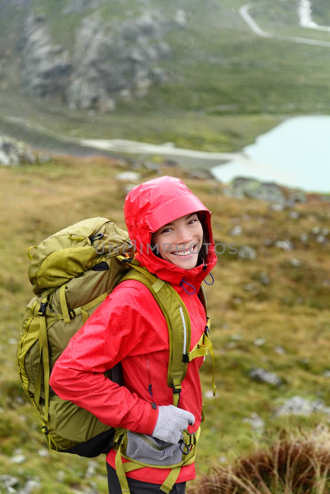 Hiker woman hiking with backpack in rain on trek living healthy active lifestyle. Smiling cheerful girl walking on hike in beautiful mountain nature landscape while raining in Swiss alps, Switzerland.