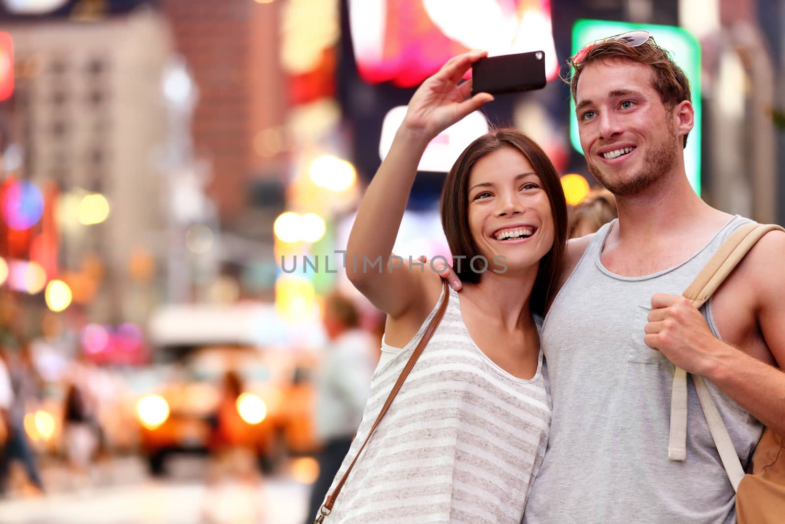 Travel tourist couple taking selfie with smartphone in New York City, USA. Self-portrait photo on Times Square at night. Beautiful young tourists having fun, Manhattan, USA. Asian woman, Caucasian man