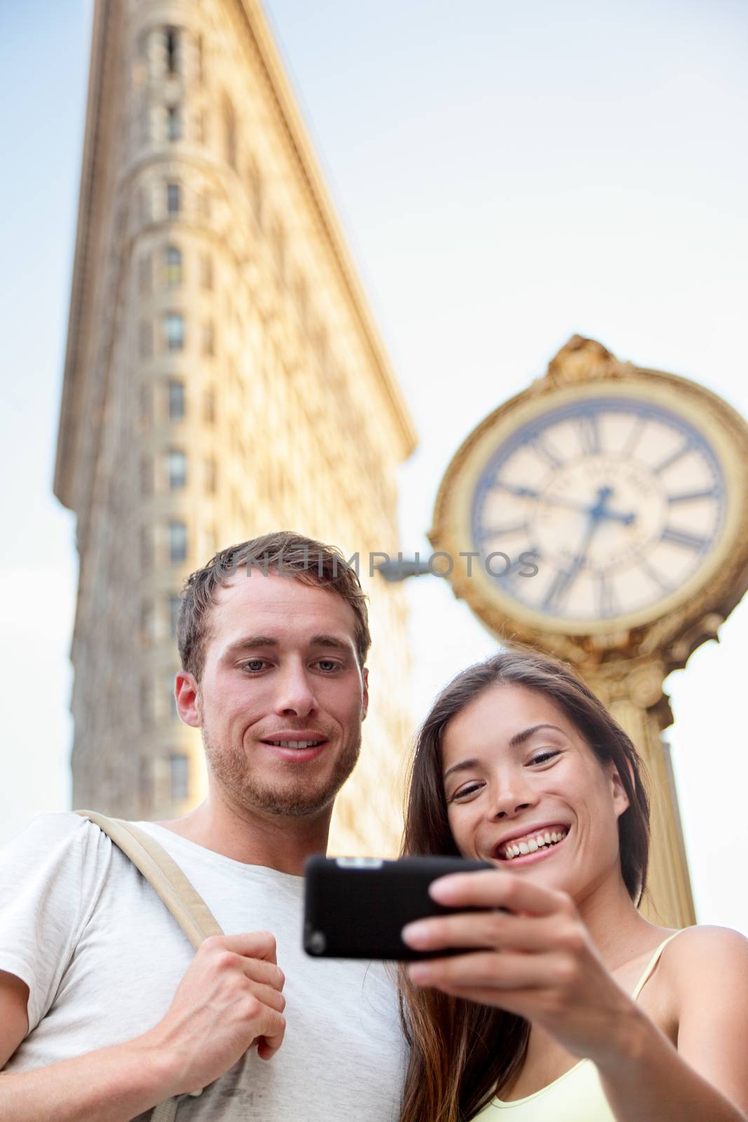 Travel couple taking selfie in New York City NYC, USA. Tourists holding smartphone to photograph self-portrait in front of famous Flatiron building downtown in summer.