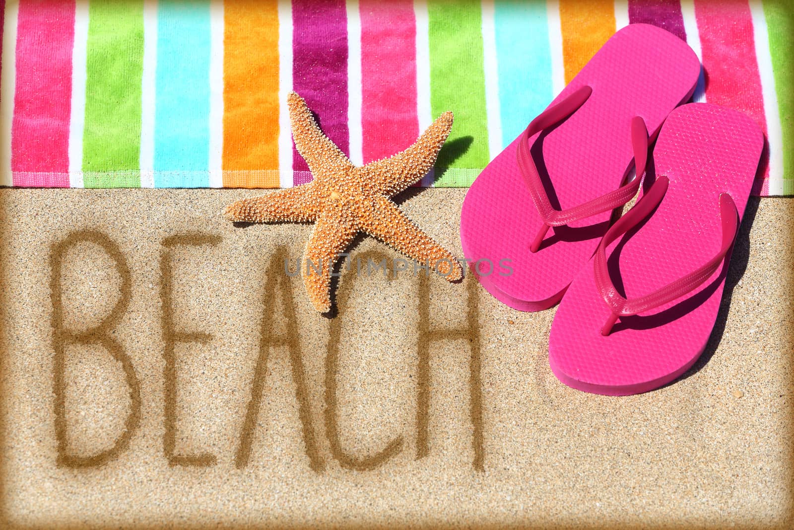 Beach vacation concept - word written on golden sand with a starfish, pink flip flops and towel conceptual of a summer vacation and travel to a sunny destination for a relaxing suntan.