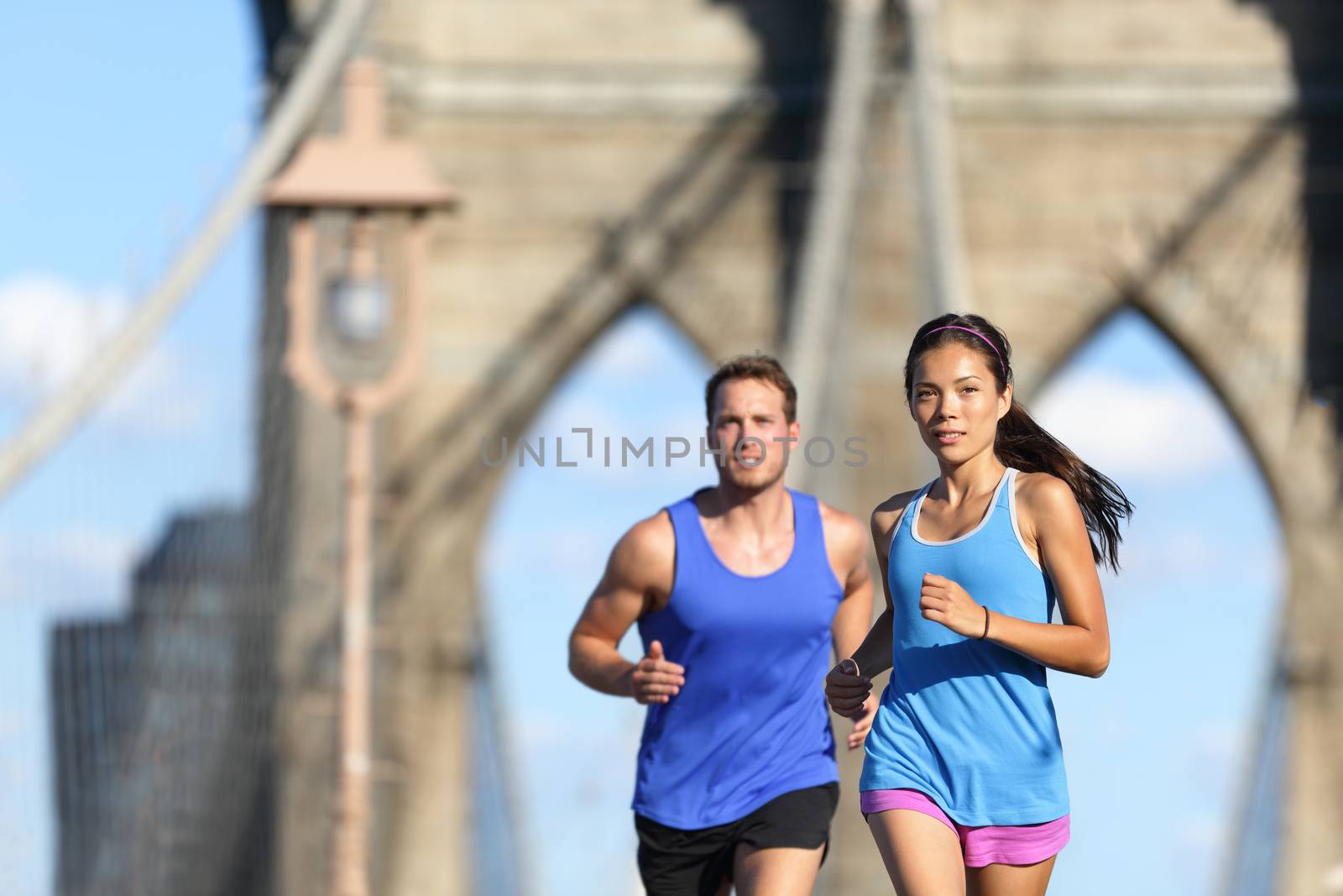 New York city runners running training for marathon on Brooklyn bridge NYC in urban cityscape. Fit young couple doing their workout routine on a summer day.