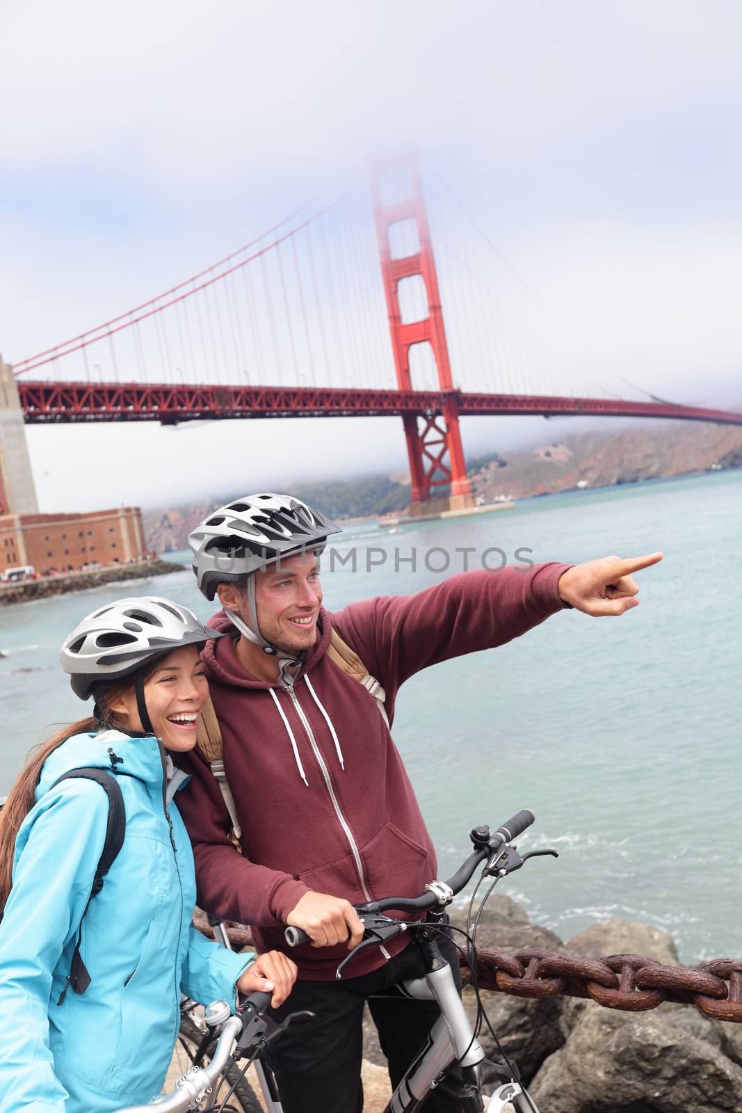 Golden gate Bridge - happy biking couple sightseeing in San Francisco, USA. Portrait of young couple tourists on bike tour enjoying the view at the famous travel landmark in California, USA.