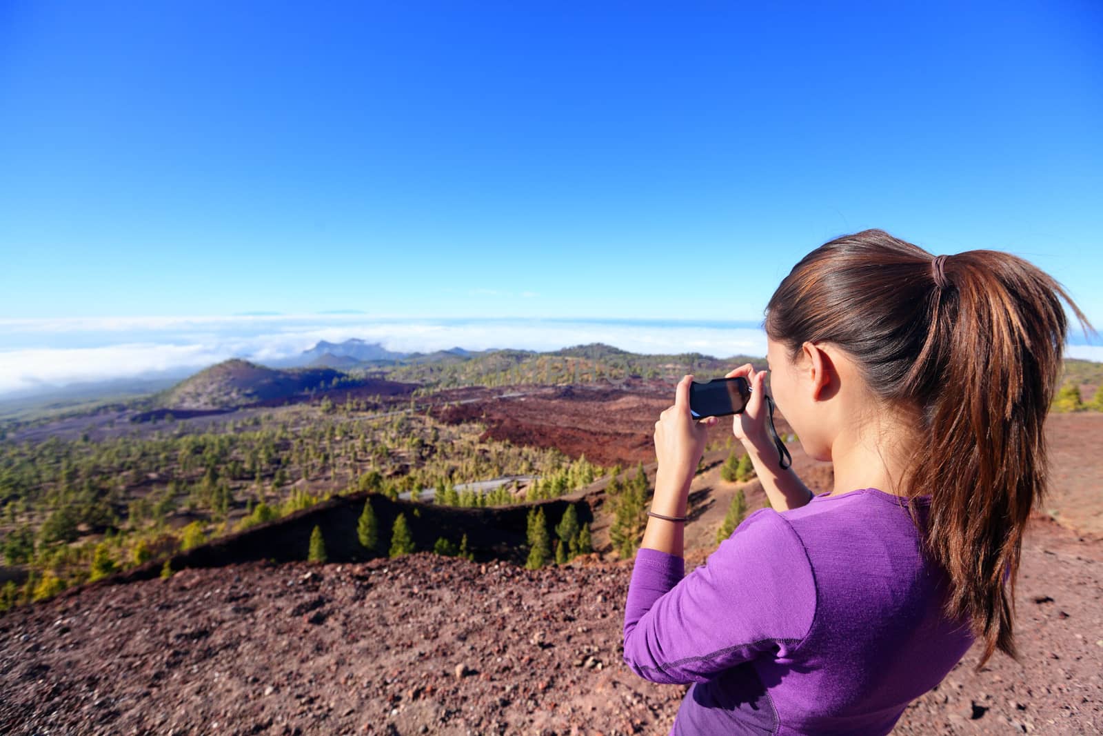Hiker taking landscape picture on top of mountain. Beautiful nature on the volcano Teide, Tenerife, Canary islands with girl tourist using smartphone to take photos.