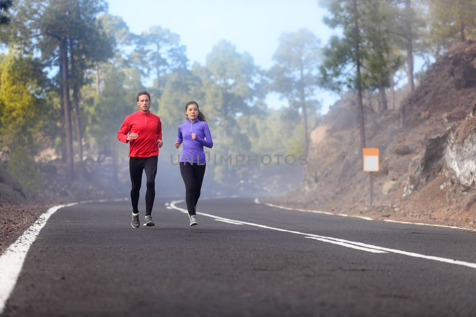 People running - athlete runners training jogging in cloudy and cold weather. Exercising runner couple working out living healthy lifestyle training for marathon together on mountain road.