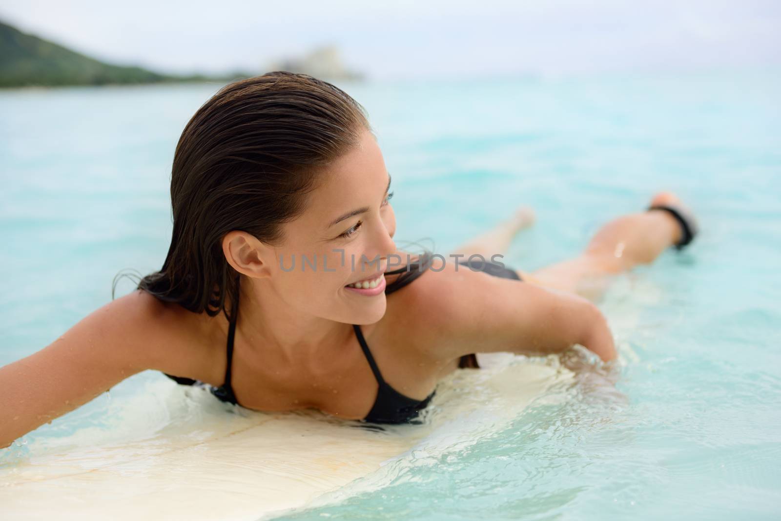 Surfing surfer girl paddle for surf on surfboard. Female bikini woman living healthy active water sports lifestyle on Hawaiian beach. Asian Caucasian model on Waikiki Beach, Oahu, Hawaii.