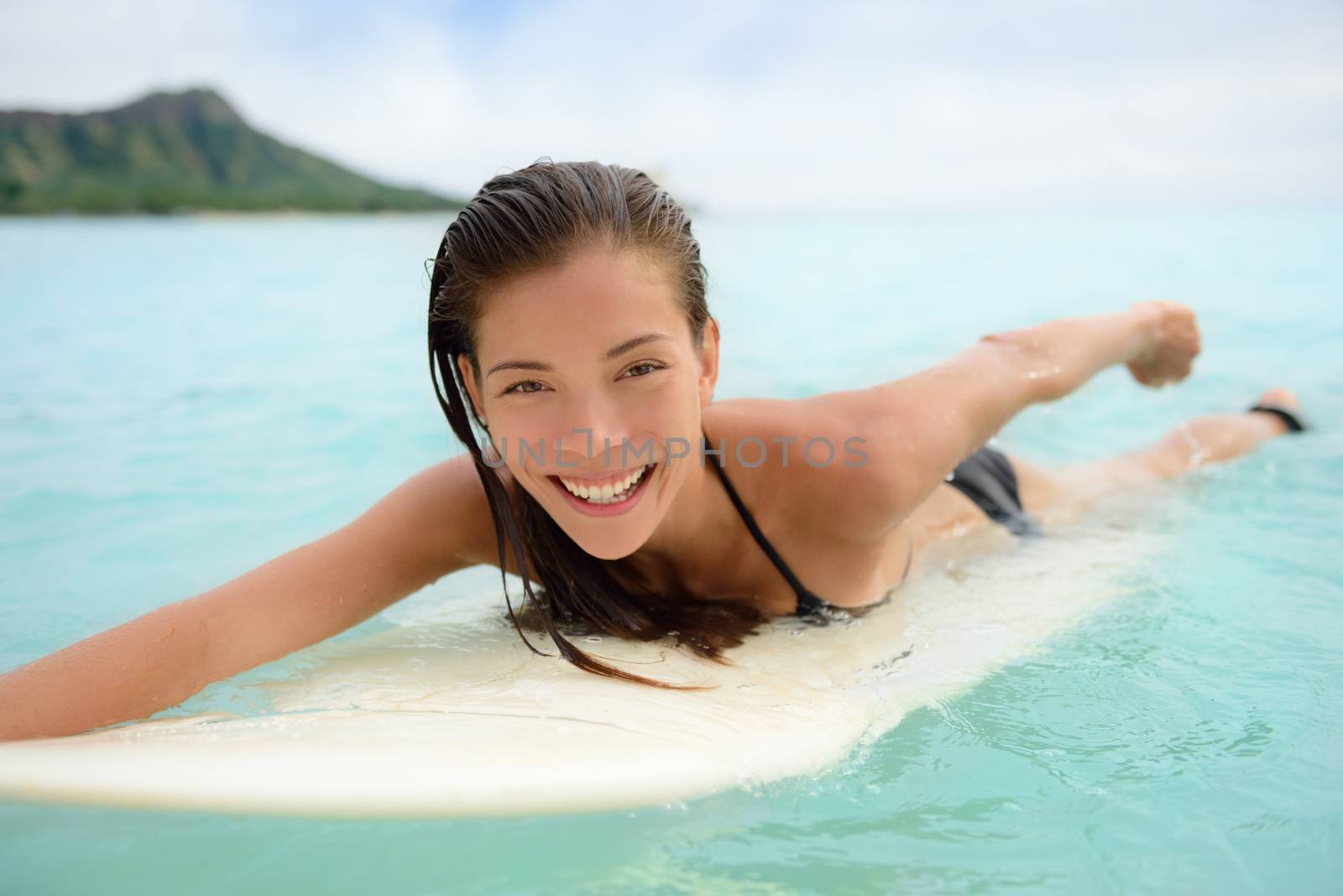 Portrait of surfer woman surfing having fun on Waikiki Beach, Oahu, Hawaii. Female bikini girl laughing on surfboard smiling happy living healthy lifestyle on Hawaiian beach. Asian Caucasian model.