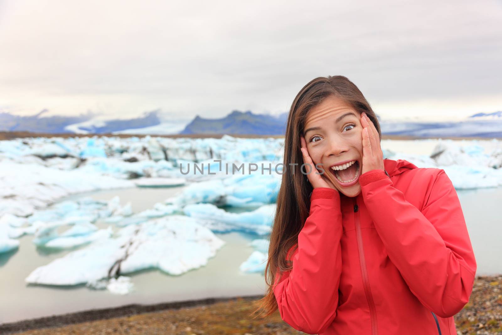 Excited happy woman at glacier lagoon on Iceland making funny face expression. Happy tourist woman by Jokulsarlon glacial lake in beautiful Icelandic nature landscape with icebergs.