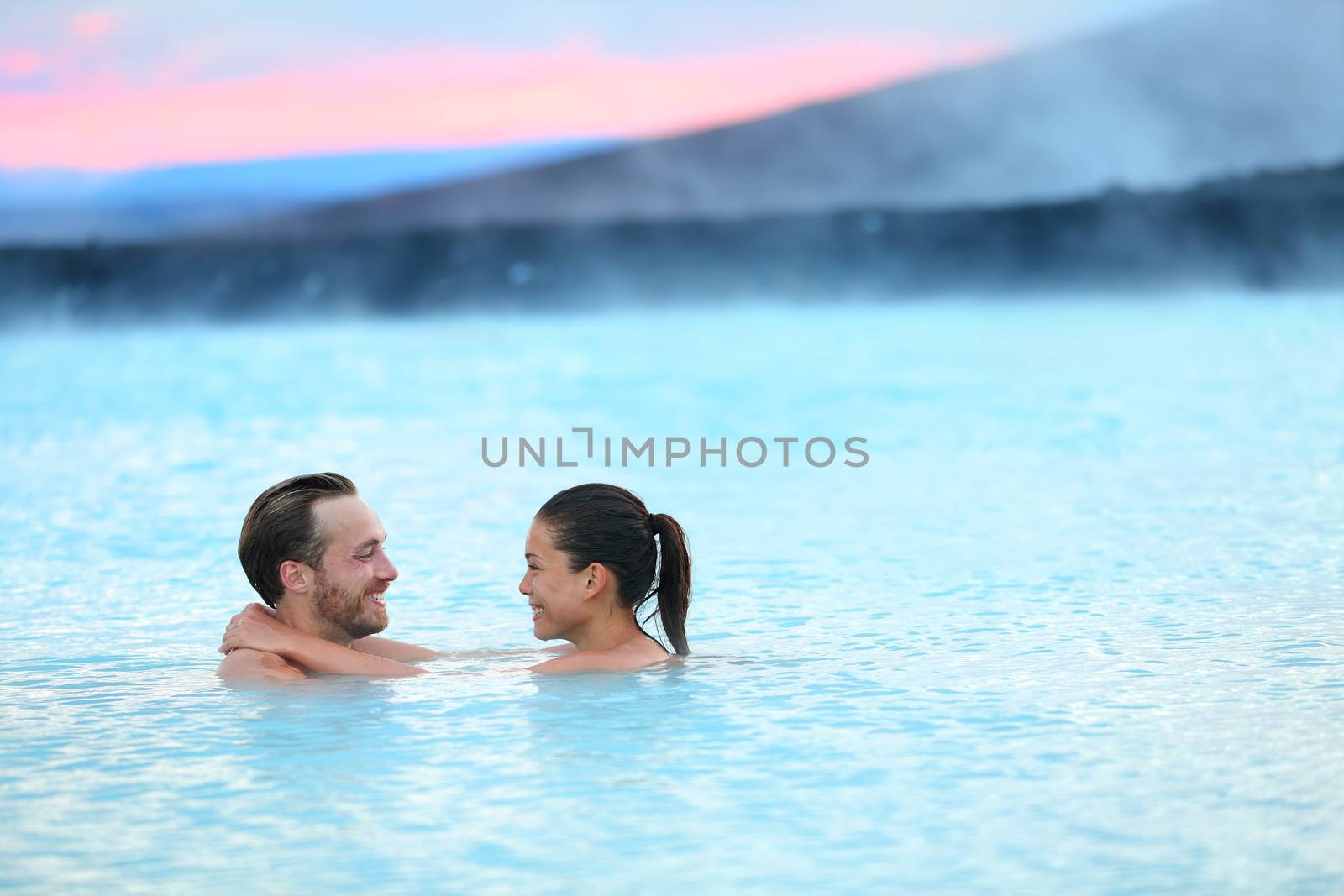 Hot spring geothermal spa on Iceland. Romantic couple in love relaxing in hot pool on Iceland. Young woman and man enjoying bathing relaxed in a blue water lagoon Icelandic tourist attraction. Sunset.