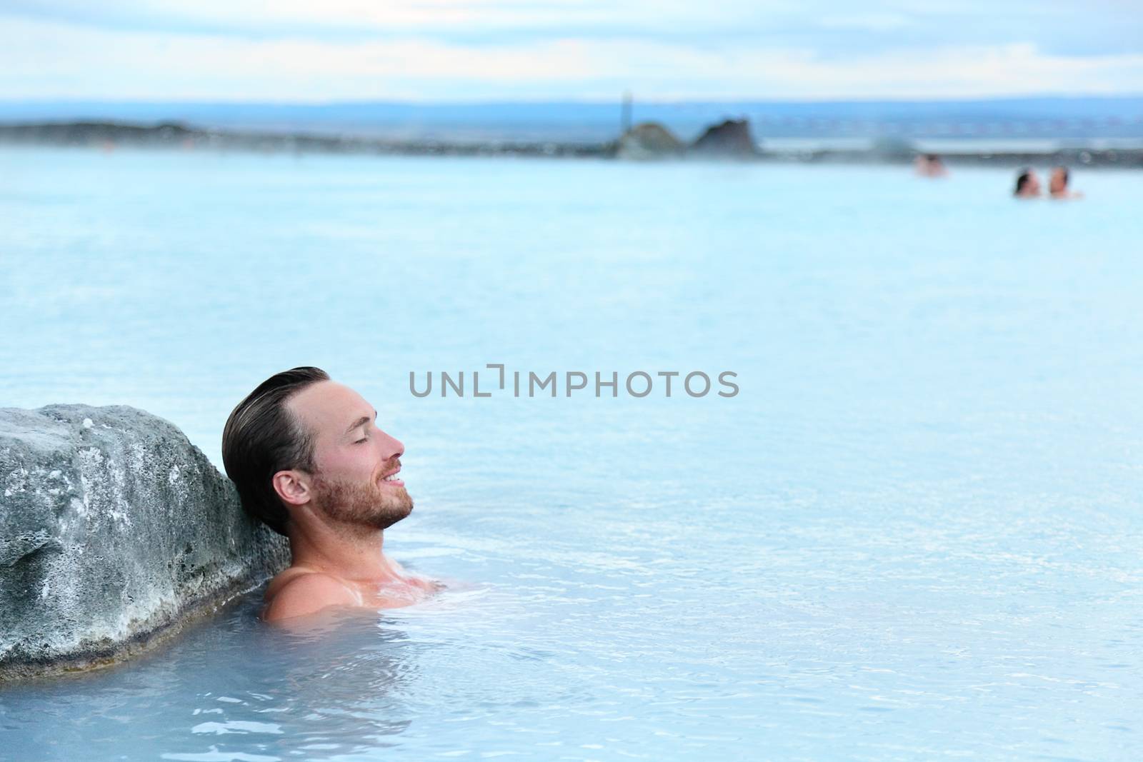 Geothermal spa. Man relaxing in hot spring pool on Iceland. Young man enjoying bathing relaxed in a blue water lagoon Icelandic tourist attraction.