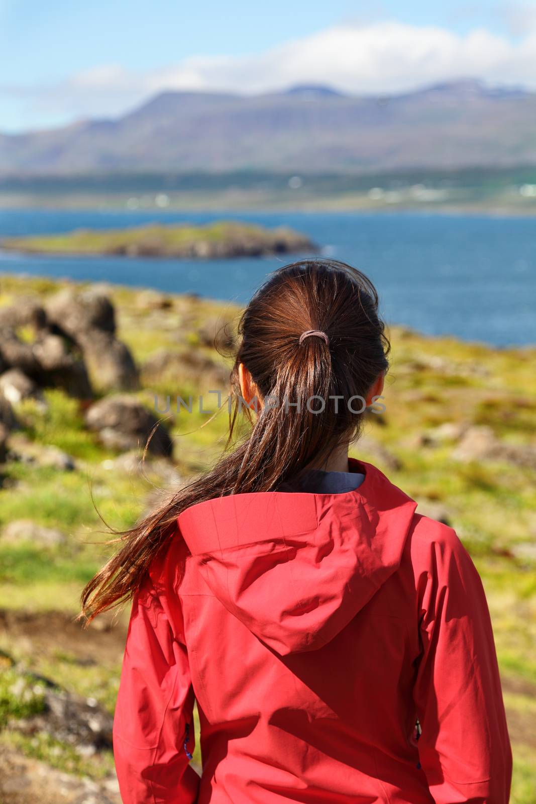 Hiking woman in hardshell jacket in Iceland nature looking at view enjoying beautiful scenic landscape on hike. Healthy active lifestyle concept with woman looking away showing backside.