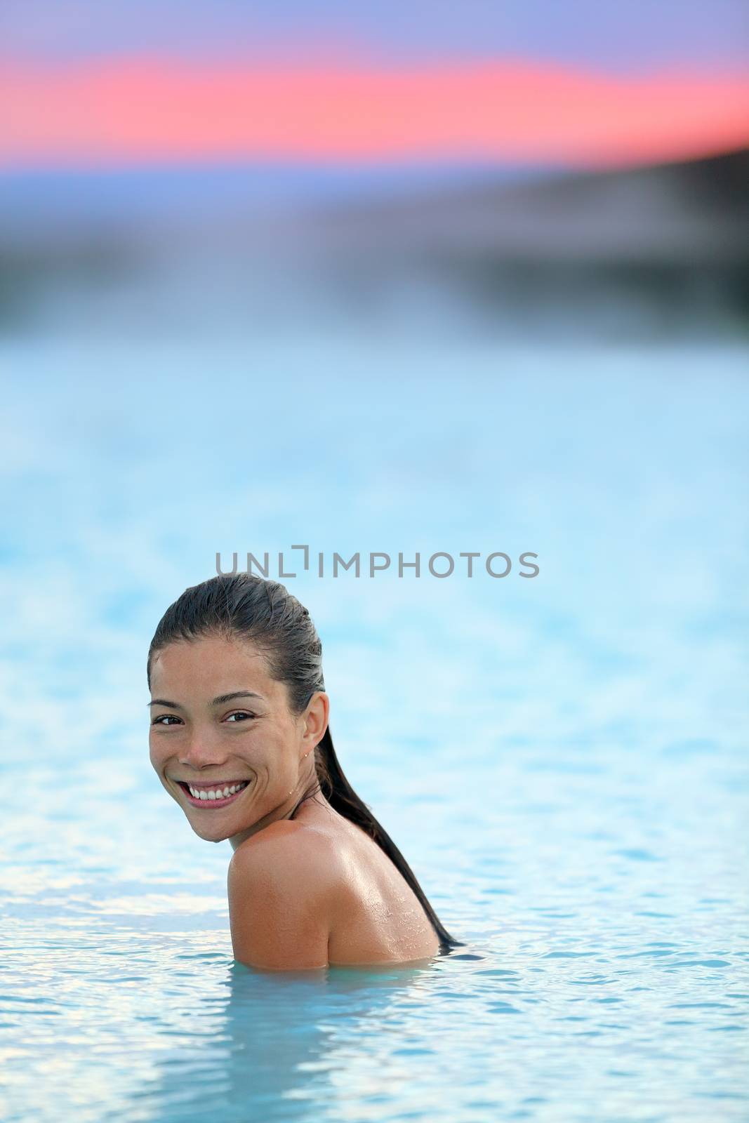 Geothermal spa. Woman relaxing in hot spring pool on Iceland. Girl enjoying bathing in a blue water lagoon Icelandic tourist attraction. Portrait of mixed race Asian Caucasian female model at sunset.