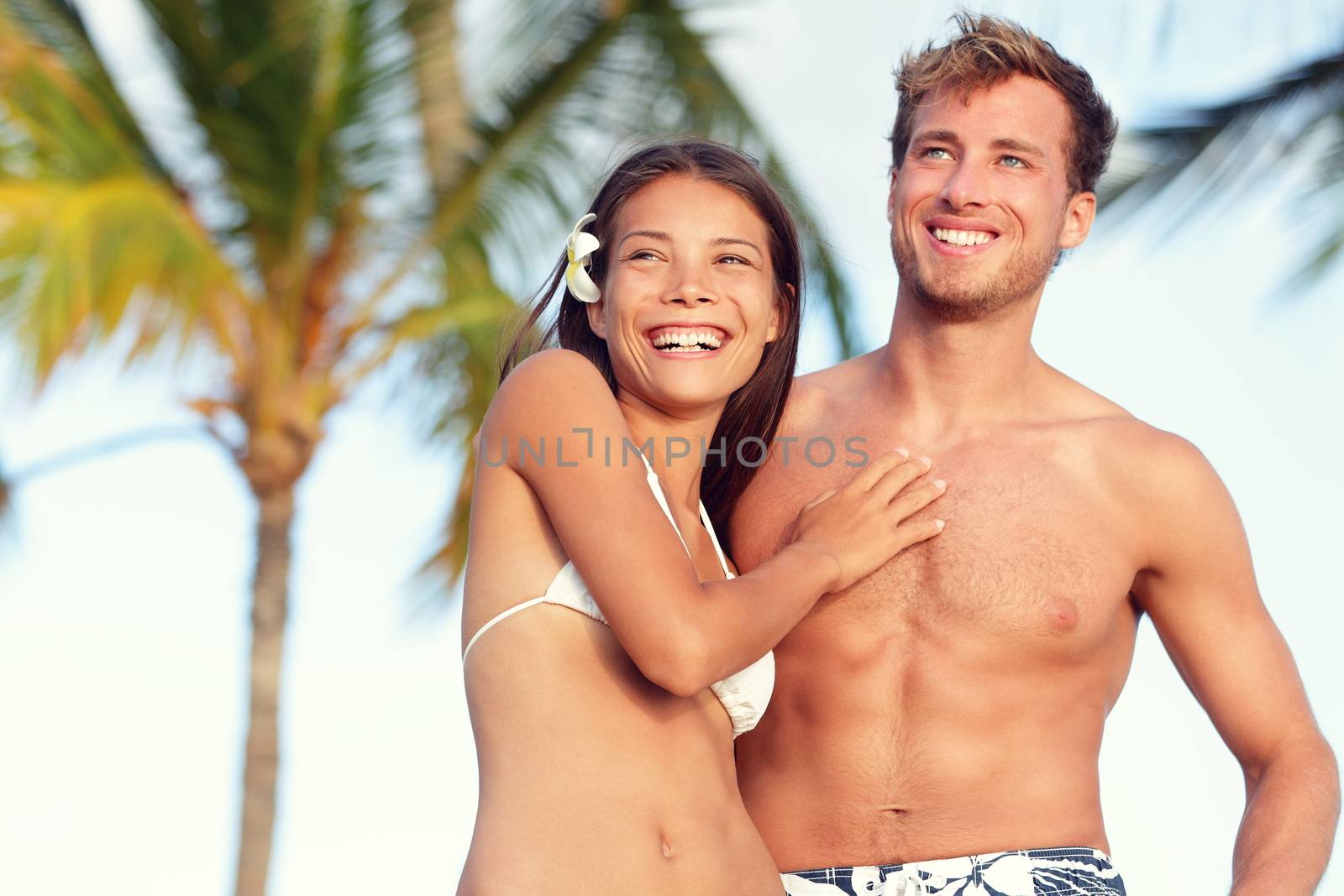 Suntan fit body couple beach travel portrait. Handsome Caucasian man and good looking Asian woman fitness young adults with tanned skin for weight loss concept or beach vacation holidays.