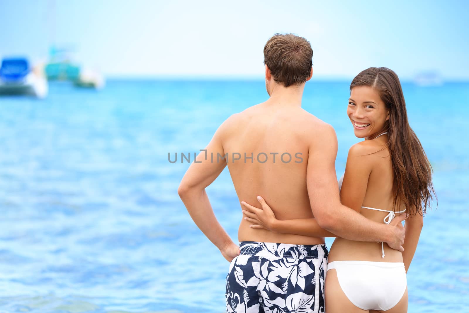 Couple beach portrait happy woman in relationship. Young Asian woman looking back at camera confident of her lover or having a secret to share, on tropical vacation.