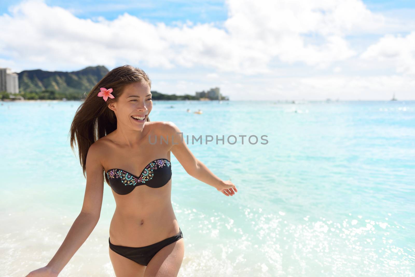Hawaii woman in bikini swimming on Hawaiian beach. Cheerful young Asian girl playing in water enjoying her summer holidays in Waikiki beach, Honolulu, Oahu, Hawaii with Diamond Head in the background.