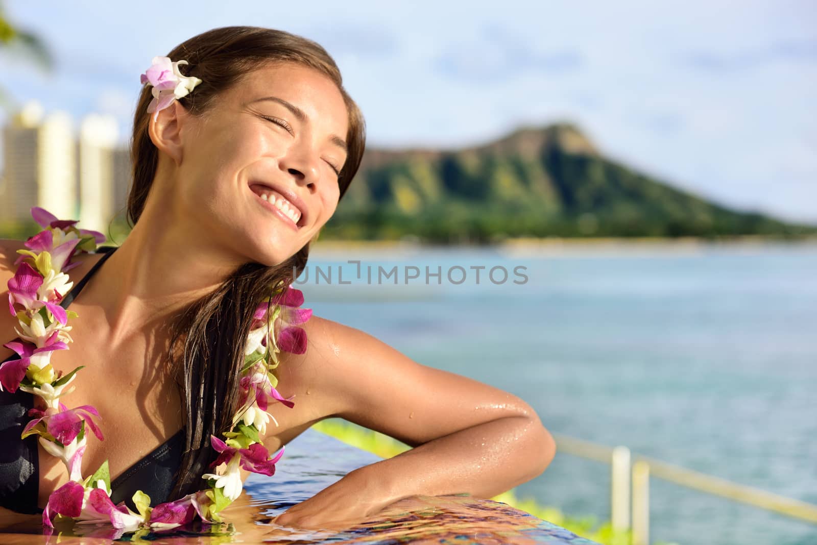 Holiday woman relaxing enjoying sun at pool resort. Peaceful young lady with closed eyes feeling the sun rays on her skin during suntan in infinity pool at beach hotel in Waikiki, Honolulu, Hawaii.