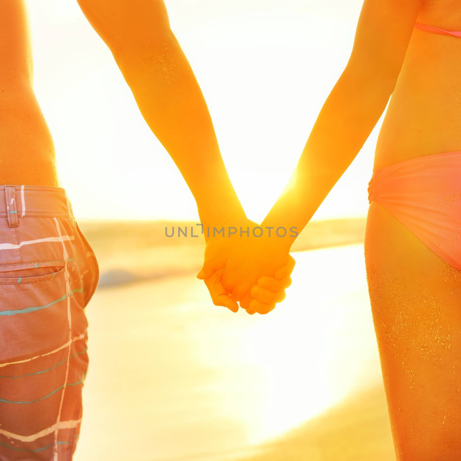 Holding hands couple in swimwear at beach. Rear view of fit couple's buttocks and legs as weight loss concept at beach sunset during summer vacations.