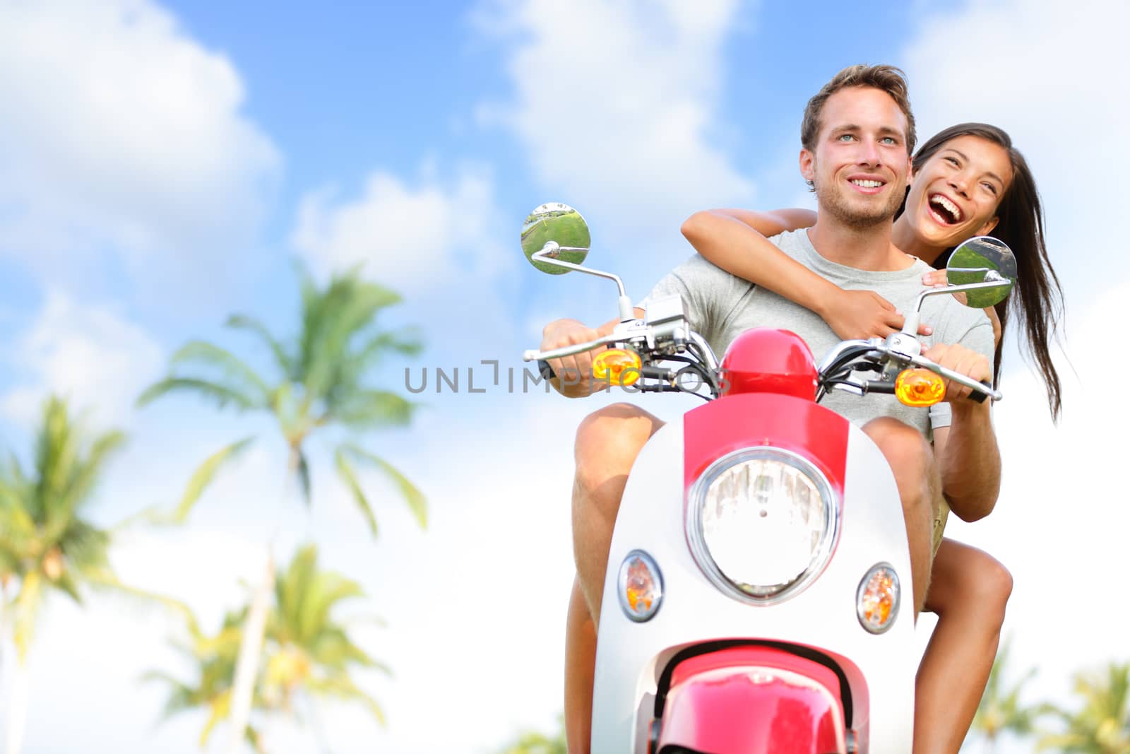 Free young couple on scooter happy on summer vacation holidays. Multiethnic cheerful couple having fun driving scooter together outdoors. Lifestyle image with Caucasian man, Asian woman.