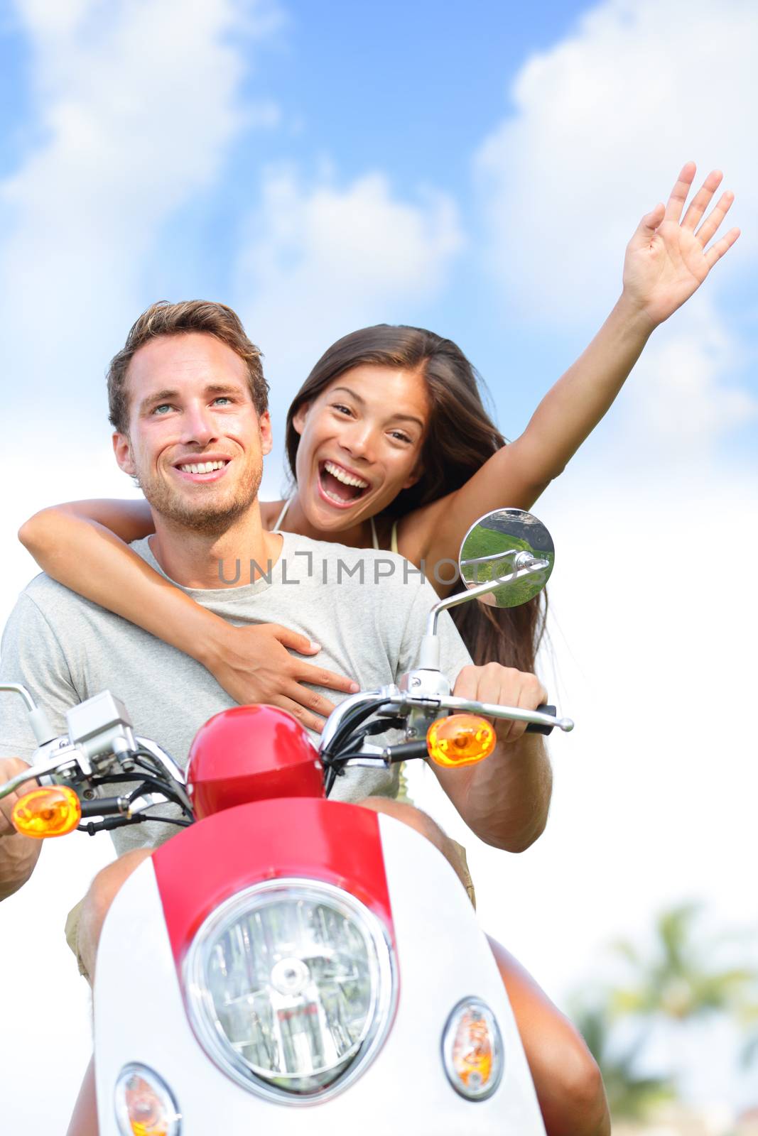 Couple driving scooter having fun in love and happy together. Joyful mixed race young couple together outside driving motorcycle scooter. Interracial couple, Asian woman, Caucasian man.