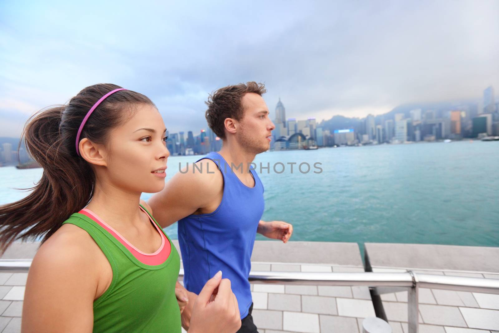 Running couple jogging in Hong Kong city. Runners training on Tsim Sha Tsui Promenade and Avenue of Stars in Victoria harbour, Kowloon, Hong Kong. Fitness runner man and sport woman model working out.
