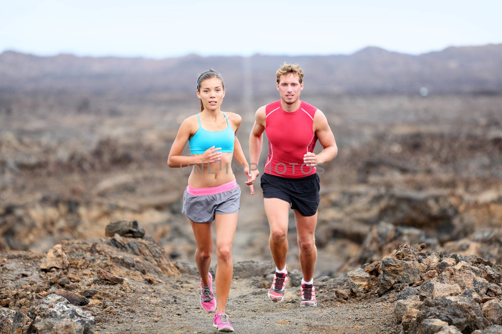 Active sport people runners on rocky trail running path outdoors training for marathon or triathlon. Fit young fitness model man and asian woman training together outside on Big Island, Hawaii, USA.