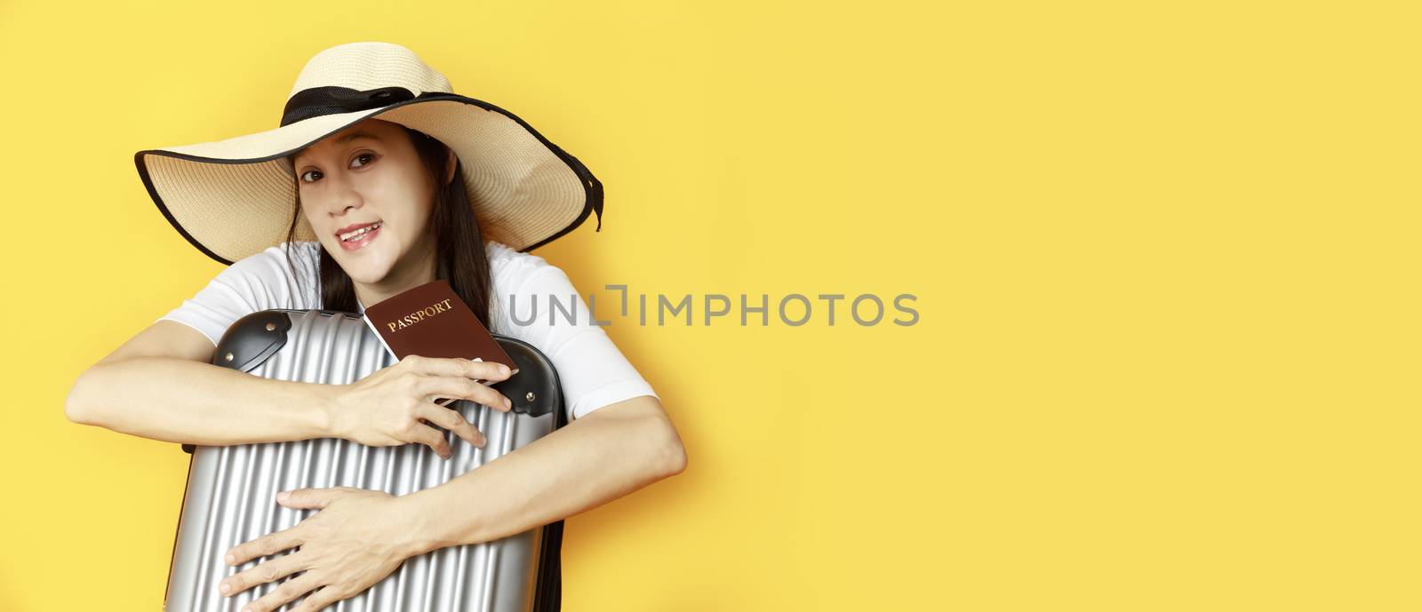 Asian women long hair wear Straw hat with black ribbon in hand holding passport book and travel bag with copy space banner. Young girl ready to travel with suitcase and passport on yellow background. Summer travel concept.