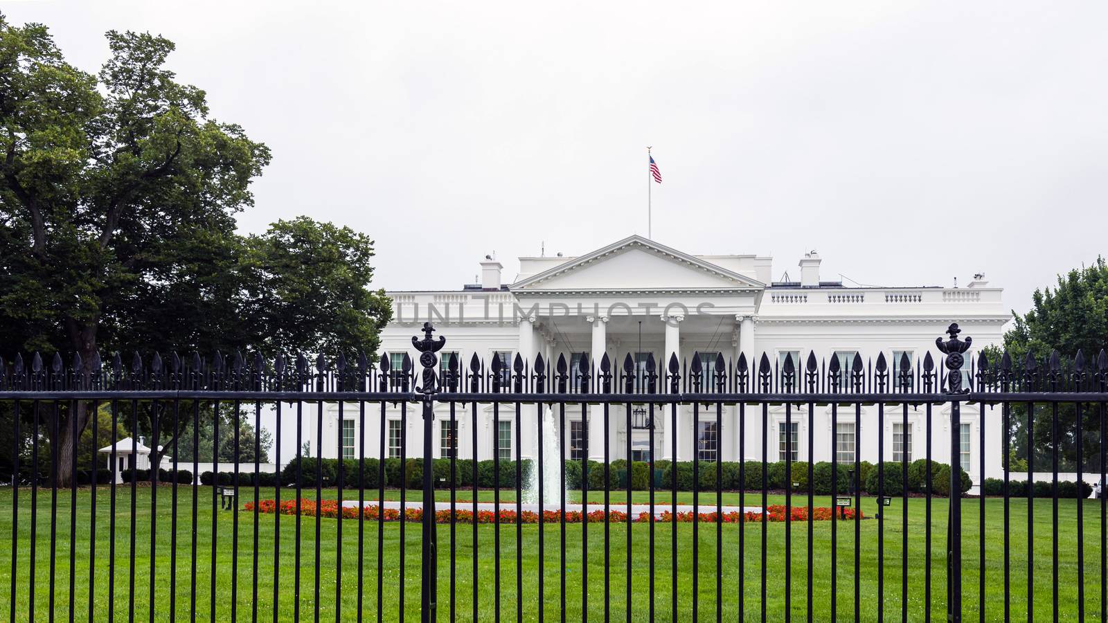 The east side of the White House with fountain, iron fence and red flowers in the foreground.